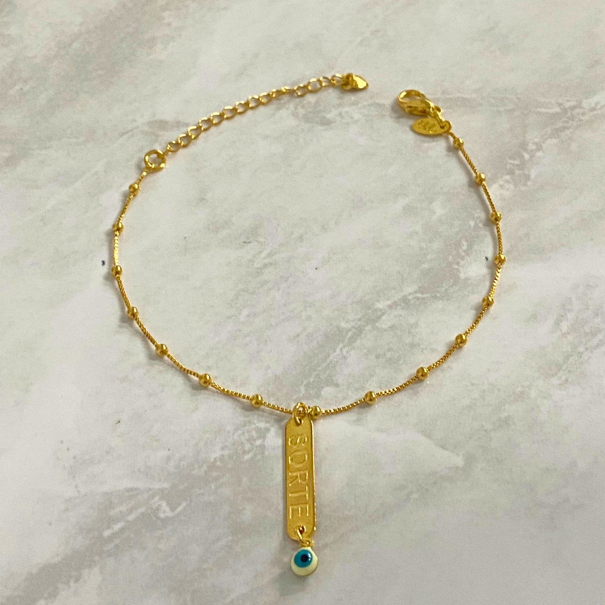PULSEIRA COM 15 BOLINHAS PP E COM UMA PLACA ESCRITO SORTE E OLHO GREGO